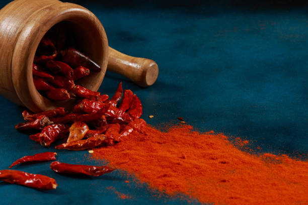 Home chilli peppers and powder with mortar and pestle on a blue stone background
